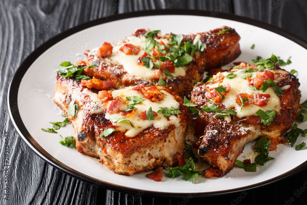 Tasty pork chops with melted parmesan and bacon closeup on a plate. horizontal