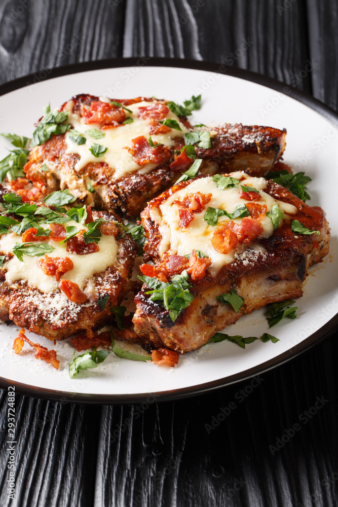 Grilled pork chops with parmesan and bacon closeup on a plate. vertical Grilled pork chops with parmesan and bacon closeup on a plate. vertical