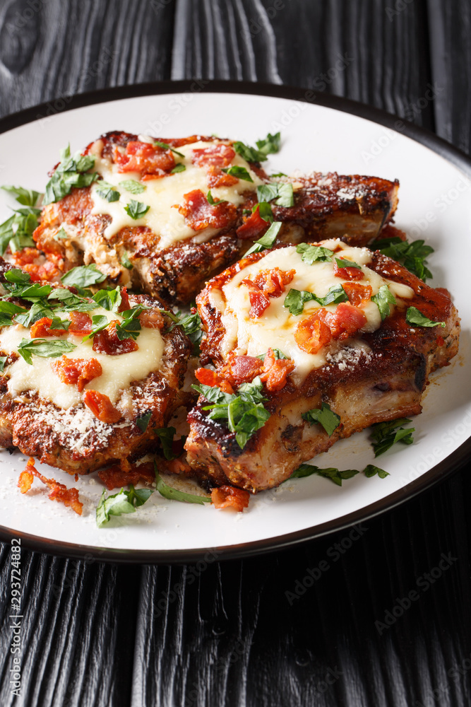 Grilled pork chops with parmesan and bacon closeup on a plate. vertical