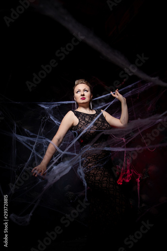 Woman in evening classic dress posing on black Halloween background with spider web