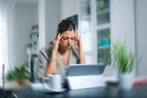 Sick dizzy young woman suffering headache while working on her laptop at home. photo