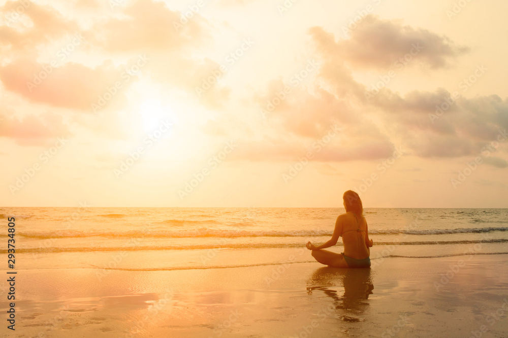 Young beautiful woman make meditation in lotus position on sunset sea beach. Solitude breathe exercise on idyllic paradise country.
