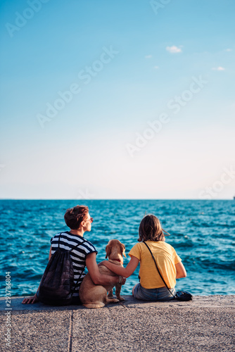Mother and daughter sitting on the waterfront with dog