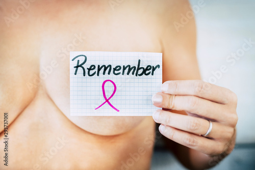 close up of nude caucasian woman holding a card of paper with written in the word remeber - concept of tumor and cancer prevention for women's day - healthy women fighting photo