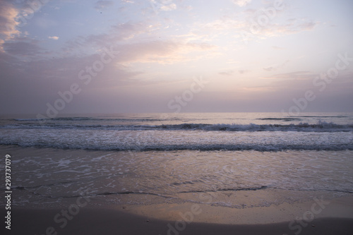 Dawn on the Mediterranean coast  Tunisia Sand in the foreground  small waves  the sun above the horizon  long clouds