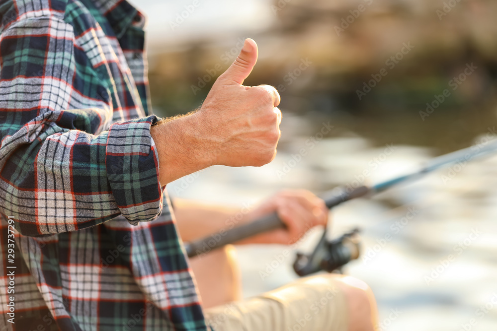Mature man showing thumb-up while fishing on river, closeup