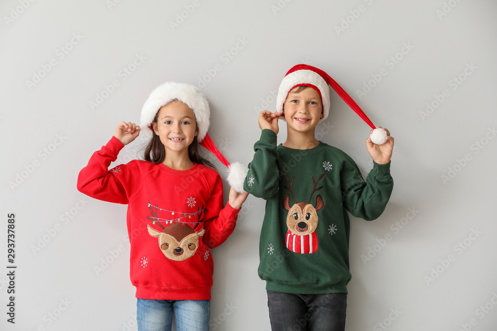Funny children in Christmas sweaters and Santa hats on light background Funny children in Christmas sweaters and Santa hats on light background