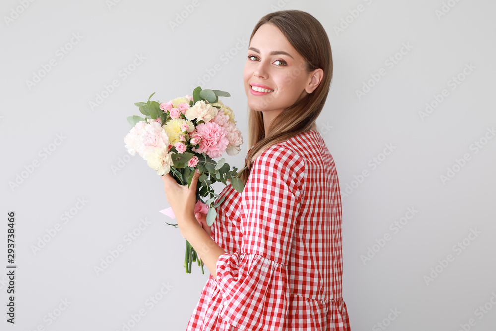 Beautiful young woman with bouquet of carnation flowers on light background