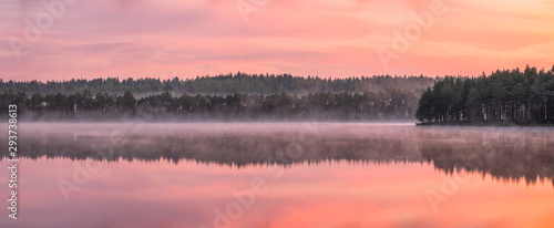 Beautiful sunrise landscape with misty mood and calm lake at foggy summer morning in Finland