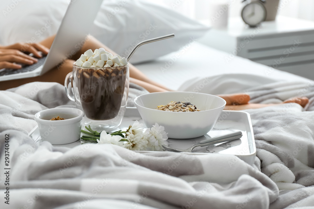 Young woman using laptop while having breakfast in bed