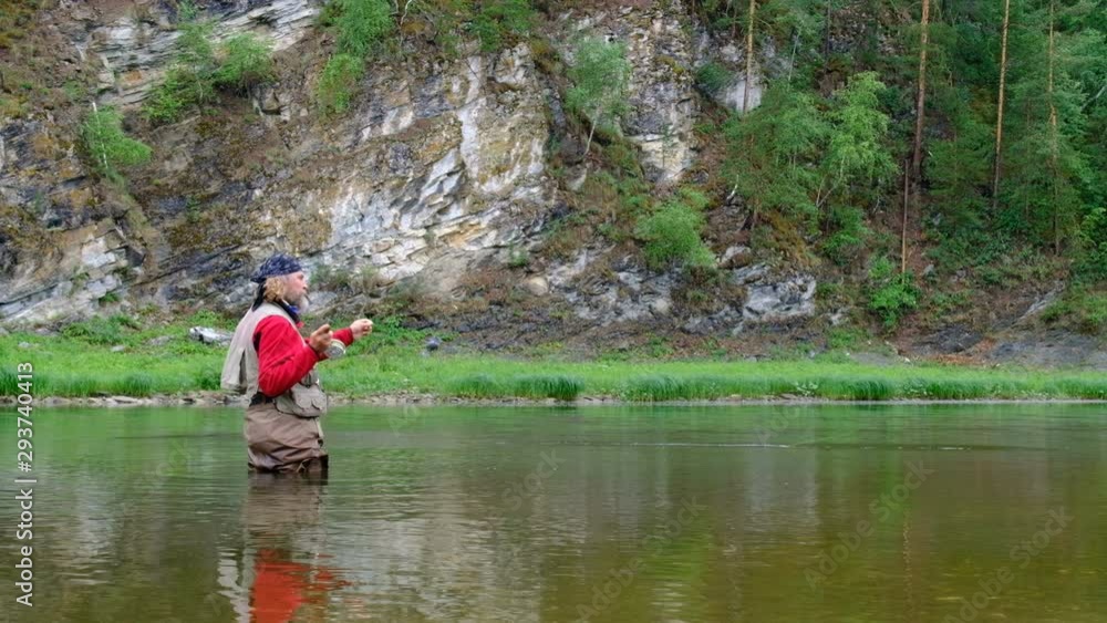 Fly fishing in a mountain river. Adult man with long hair and a Santa Claus beard holds a fishing rod. Recreation and sports in Bashkiria. Belaya river. Southern Urals. Fly fishing in a mountain river. Adult man with long hair and a Santa Claus beard holds a fishing rod. Recreation and sports in Bashkiria. Belaya river. Southern Urals.