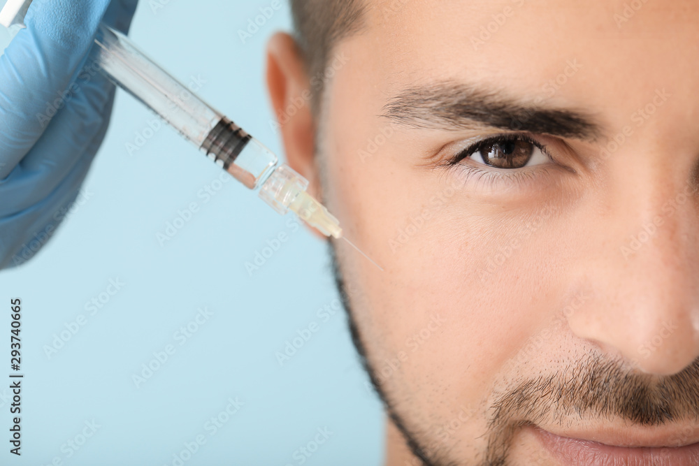 Handsome man receiving filler injection on color background, closeup Handsome man receiving filler injection on color background, closeup