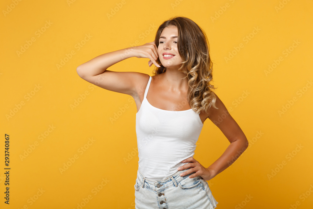 Smiling young woman in light casual clothes posing isolated on yellow orange wall background. People lifestyle concept. Mock up copy space. Looking aside, doing phone gesture like says call me back.