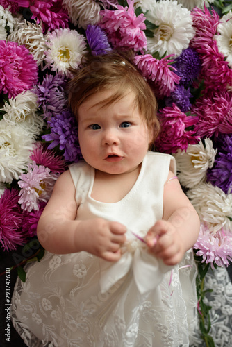 Baby girl in blue dress playing with bunch of pink tulips. Little child at home in sunny nursery. Toddler having fun with flowers