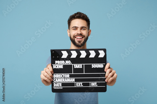 Young smiling man in casual clothes posing isolated on blue wall background, studio portrait. People lifestyle concept. Mock up copy space. Holding in hands classic black film making clapperboard.