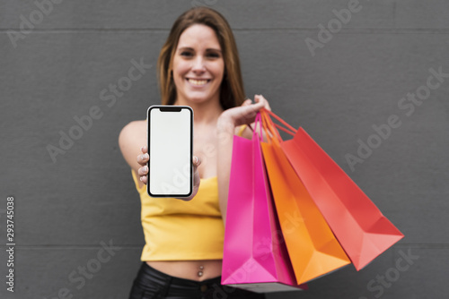 Smiling girl with shopping bags holding phone