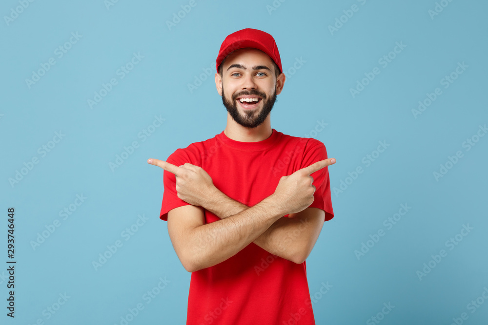 Delivery man in red uniform workwear isolated on blue wall background, studio portrait. Professional male employee in cap t-shirt print working as courier dealer. Service concept. Mock up copy space. Delivery man in red uniform workwear isolated on blue wall background, studio portrait. Professional male employee in cap t-shirt print working as courier dealer. Service concept. Mock up copy space.