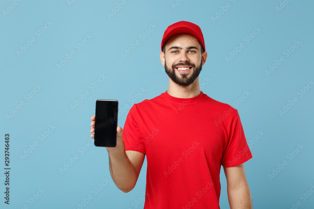 Delivery man in red uniform workwear hold cellphone isolated on blue background, studio portrait. Professional male employee in cap t-shirt working courier dealer. Service concept. Mock up copy space. Delivery man in red uniform workwear hold cellphone isolated on blue background, studio portrait. Professional male employee in cap t-shirt working courier dealer. Service concept. Mock up copy space.