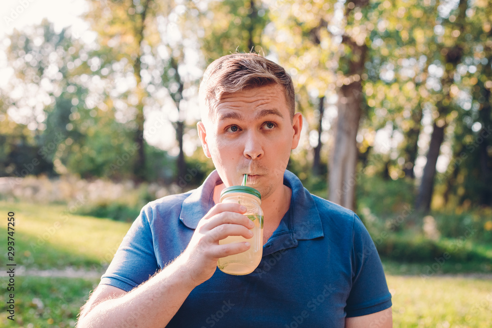 Young crazy man drinking a mojito and thinks something. A man outdoors, immersed in nature, drinks a glass of homemade lemonade. Vitamins and regular life concept Young crazy man drinking a mojito and thinks something. A man outdoors, immersed in nature, drinks a glass of homemade lemonade. Vitamins and regular life concept