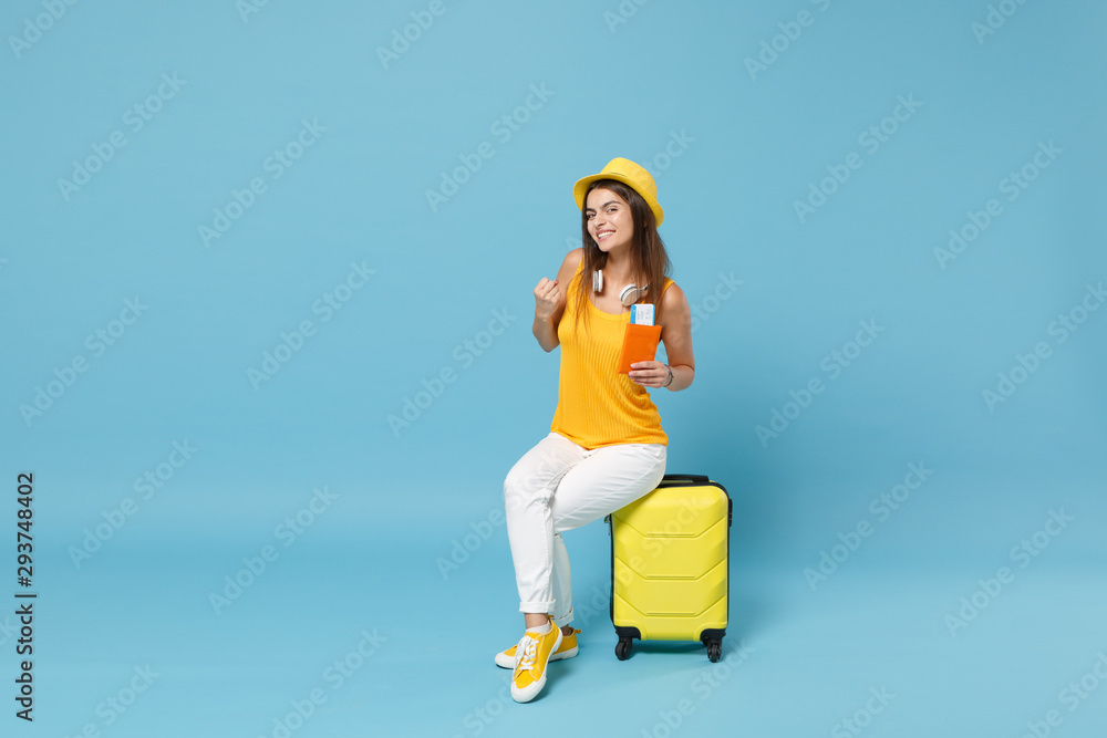 Traveler tourist woman in yellow summer casual clothes hat hold tickets luggage isolated on blue background. Female passenger traveling abroad to travel on weekends getaway. Air flight journey concept - obrazy, fototapety, plakaty 