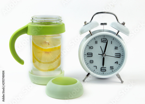Alarm clock and a detox glass of water with lemon on a glass table. Wake up early in the morning by the alarm bell.