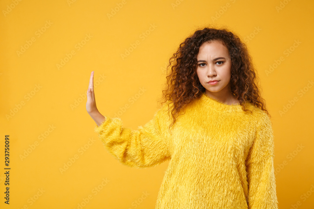 Serious young african american girl in fur sweater posing isolated on yellow orange wall background studio portrait. People lifestyle concept. Mock up copy space. Showing stop gesture aside with palm. Serious young african american girl in fur sweater posing isolated on yellow orange wall background studio portrait. People lifestyle concept. Mock up copy space. Showing stop gesture aside with palm.
