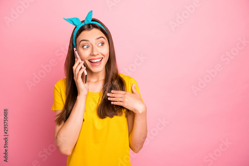 Portrait of astonished girl having dialogue using gadget wearing yellow t-shirt isolated over pink background