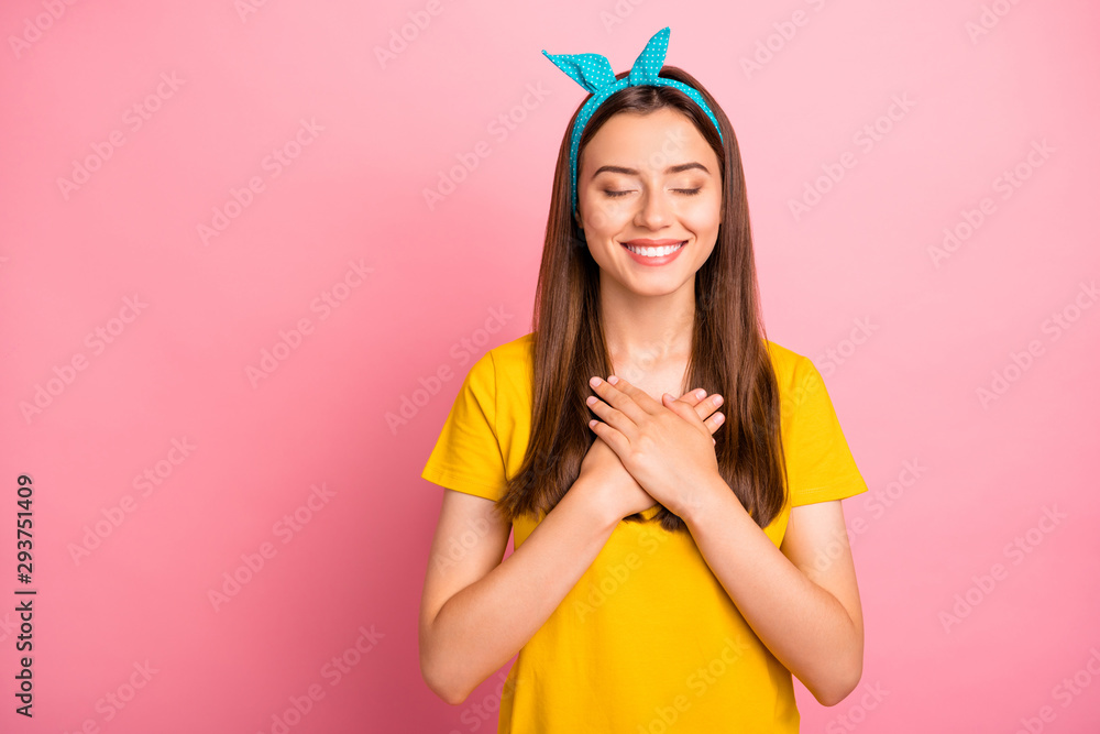 Portrait of cute hipster closing her eyes touching chest wearing yellow t-shirt isolated over pink background - obrazy, fototapety, plakaty 