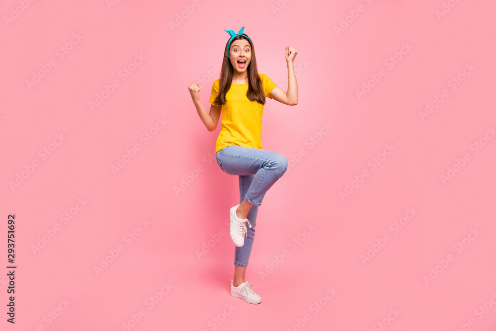 Full body photo of cheerful girl raising fists screaming wow omg yeah wearing yellow t-shirt isolated over pink background