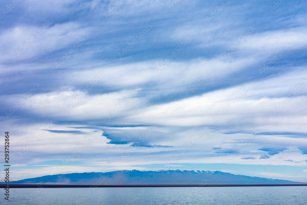 panoramic view of blue sky with white fluffy clouds reflecting on water surface of amazing lake with mountains on background 