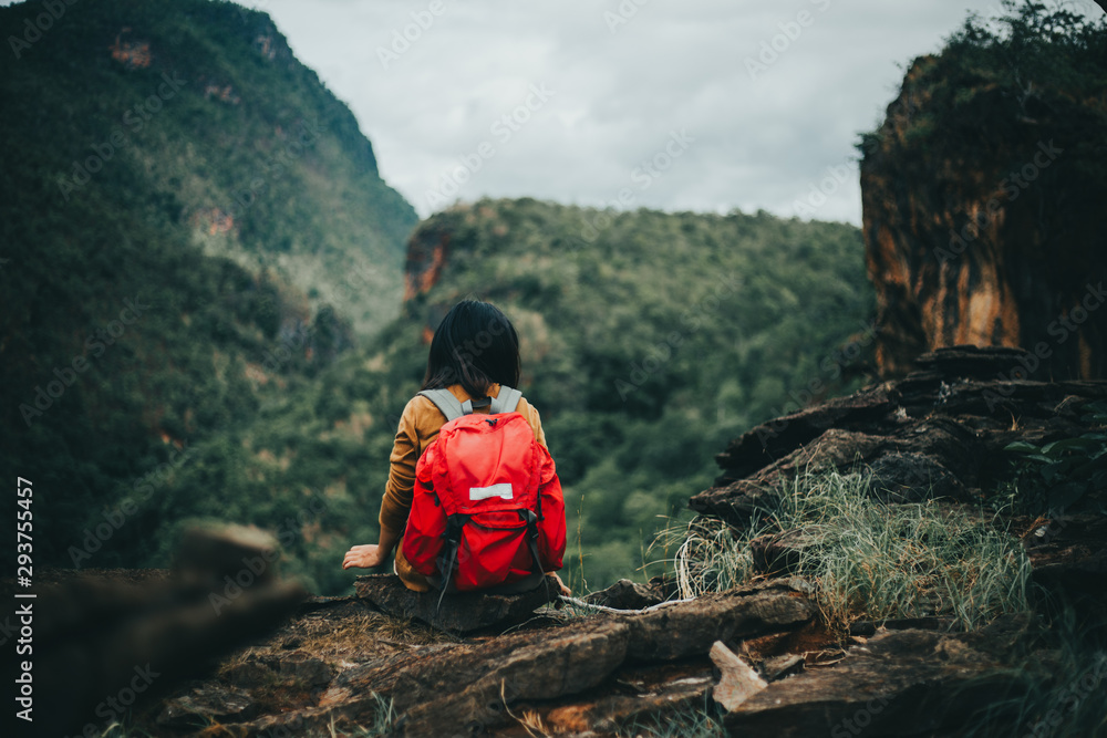 Behind hipster young girl with red backpack on peak mountain. Traveling alone concept.
