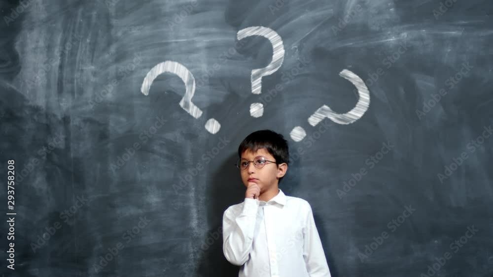 Little schoolboy in white shirt and eyeglasses standing against blackboard with animated chalk drawings of question marks, rubbing his chin and thinking about something Little schoolboy in white shirt and eyeglasses standing against blackboard with animated chalk drawings of question marks, rubbing his chin and thinking about something