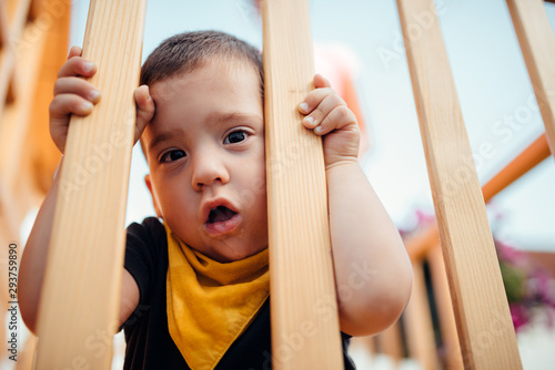 Toddler boy looking through wooden fence on playground