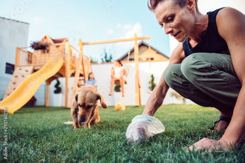 Фотография Woman picking up dog poop from the lawn