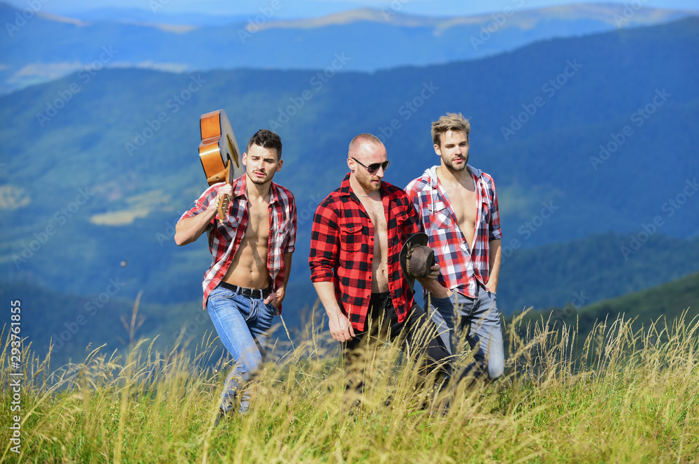Tourists hiking concept. Group of young people in checkered shirts walking together on top of mountain. Men with guitar hiking on sunny day. Hiking with friends. Long route. Enjoying freedom together