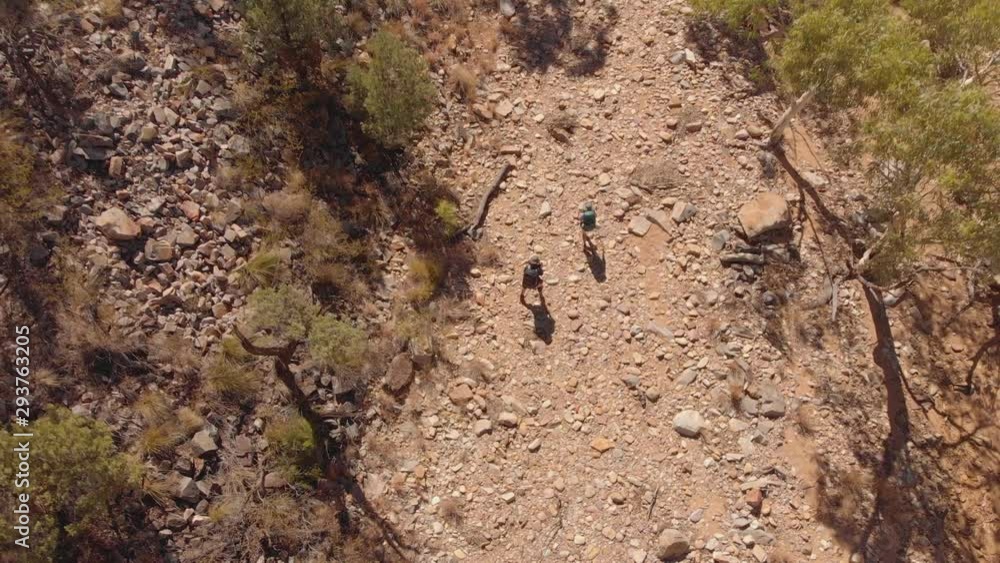 Aerial rising reveal of people hiking dry river bed through mountain range Aerial rising reveal of people hiking dry river bed through mountain range