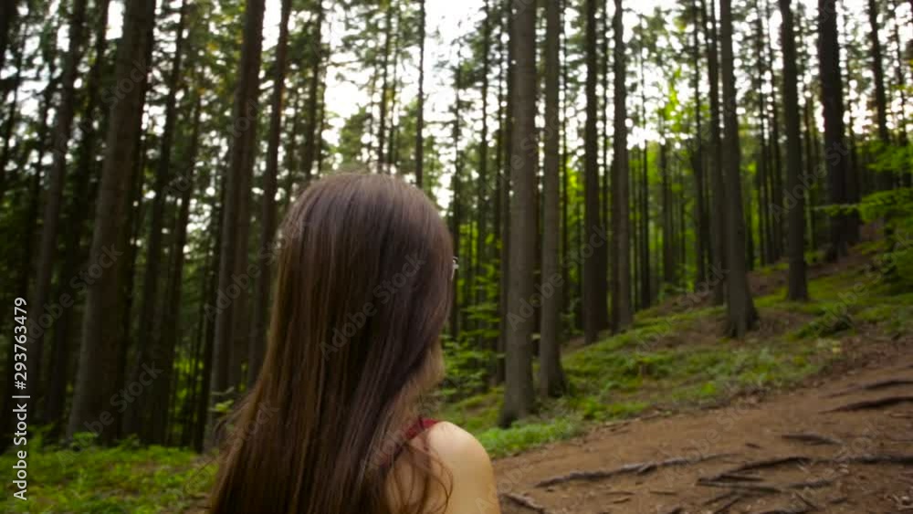 Slow motion shot starting to circle a brown-haired woman standing in the middle of a thick forest. Slow motion shot starting to circle a brown-haired woman standing in the middle of a thick forest.