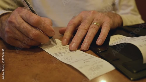 Close Up of a Married Male Senior Citizen's Hands Signing the Bill at a Restaurant, while wearing a gold ring and a white dress shirt photo