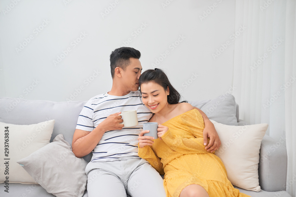 Affectionate couple holding coffee cups sitting on a sofa in the living room at home Affectionate couple holding coffee cups sitting on a sofa in the living room at home