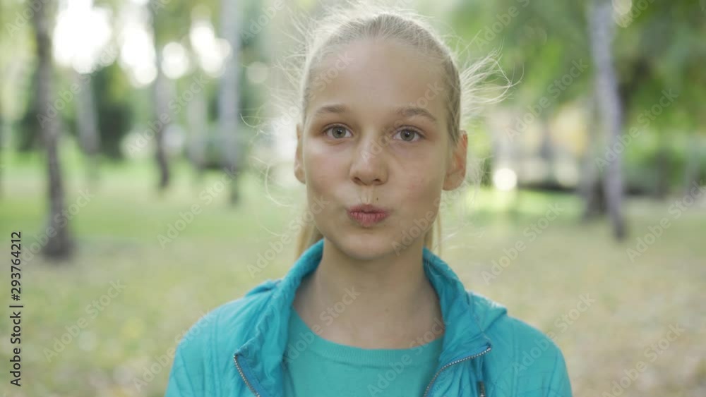 Portrait of a young blond girl looking at the camera. Pretty caucasian teen standing in the sunny park and smiling. Portrait of a young blond girl looking at the camera. Pretty caucasian teen standing in the sunny park and smiling.