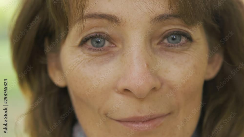Extreme close-up of nice brunette grey-eyed caucasian woman standing in the sunny park and smiling to the camera. Beautiful lady enjoying last warm days of the autumn. Extreme close-up of nice brunette grey-eyed caucasian woman standing in the sunny park and smiling to the camera. Beautiful lady enjoying last warm days of the autumn.