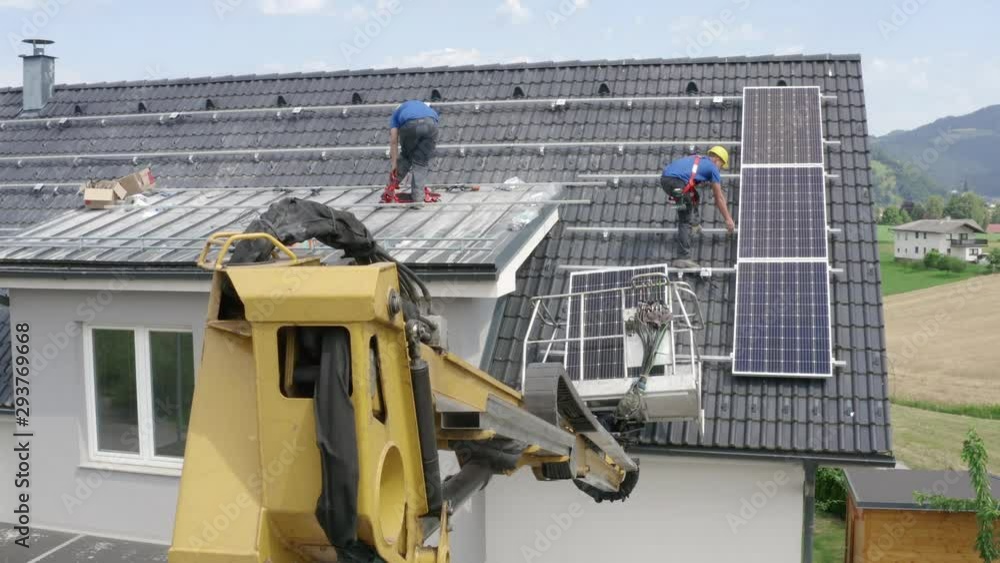Two guys mounting a solar panels on the roof - one of them is putting on a safety harness. ORBITAL shot to the right Two guys mounting a solar panels on the roof - one of them is putting on a safety harness. ORBITAL shot to the right