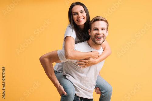 beautiful happy couple piggybacking in white t-shirts, isolated on yellow