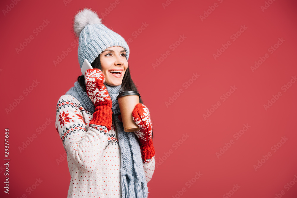 attractive woman in winter clothes talking on smartphone and holding coffee to go isolated on red attractive woman in winter clothes talking on smartphone and holding coffee to go isolated on red