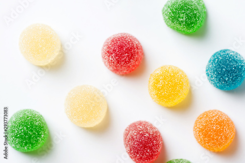 Colorful yellow red orange green gummy jelly candies coated with sugar on white background. Kids birthday party Halloween sweets fun concept. Creative minimalist food poster top view. Blurry photo