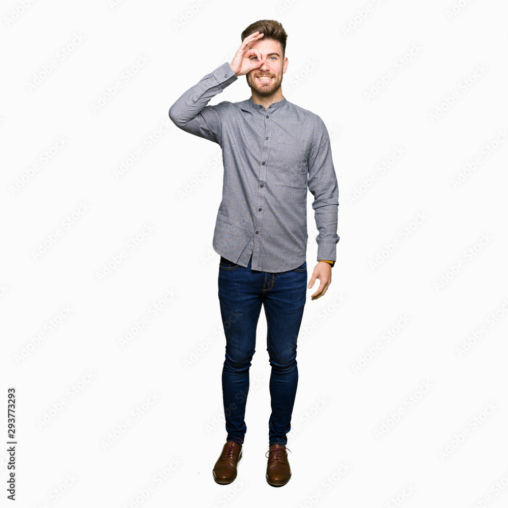 Young handsome business casual man doing ok gesture with hand smiling, eye looking through fingers with happy face. Young handsome business casual man doing ok gesture with hand smiling, eye looking through fingers with happy face.