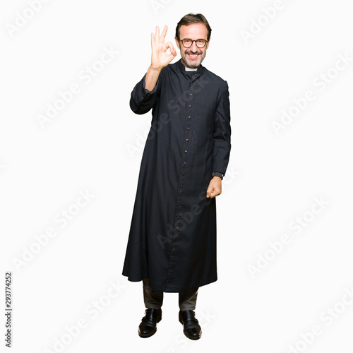 Middle age priest man wearing catholic robe smiling positive doing ok sign with hand and fingers. Successful expression.