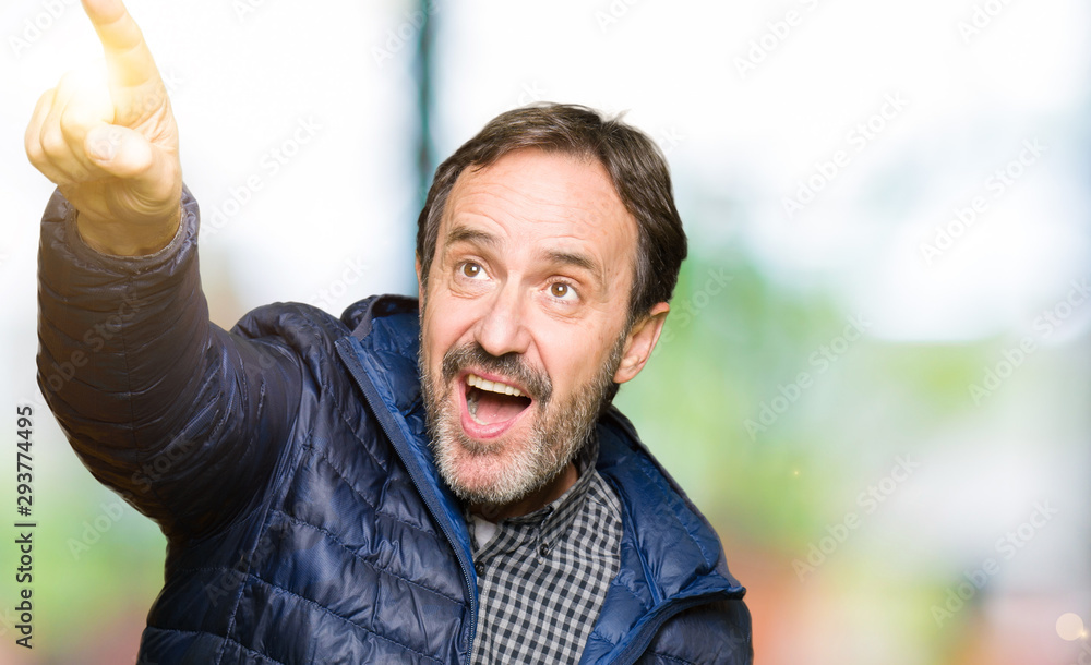 Middle age handsome man wearing winter coat Pointing with finger surprised ahead, open mouth amazed expression, something in front Middle age handsome man wearing winter coat Pointing with finger surprised ahead, open mouth amazed expression, something in front