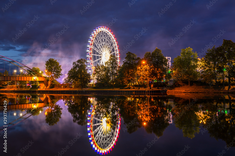 Germany, Colorful illuminated ferris wheel and lights of giant swabian fair called cannstatter wasen in stuttgart city by night reflecting in neckar river water