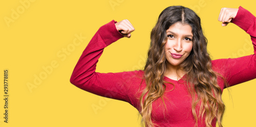 Young beautiful woman wearing red sweater showing arms muscles smiling proud. Fitness concept.